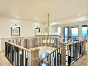 Upper-level landing featuring a gold-toned chandelier, recessed lighting, and a light wood-finish banister with black metal spindles