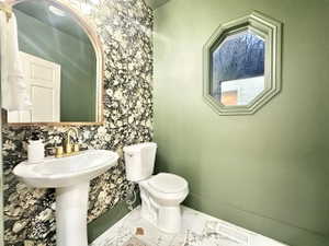 Powder room featuring a pedestal sink with gold-tone fixtures, an arched mirror, and floral pattern wallpaper