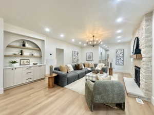 Spacious living area featuring light wood-finish flooring, a stone fireplace with a substantial hearth, built-in cabinetry with an arched display niche and floating shelves, recessed lighting, and a contemporary chandelier