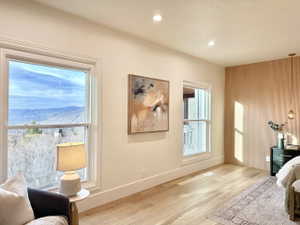 Light wood-finish flooring, recessed ceiling lighting, two windows with white trim, and a decorative slatted wood accent wall