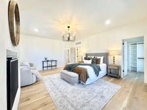 Spacious sleeping area featuring light wood-finish flooring, a contemporary chandelier, recessed lighting, a modern fireplace, and a built-in closet system