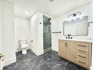 Modern bathroom featuring black marbled tile flooring, a sleek glass-enclosed shower with textured tile, a light wood-finish vanity with ample storage, a white countertop, and a contemporary black-framed mirror with multi-bulb lighting