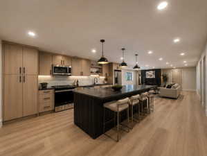 Open-concept kitchen featuring light wood-finish cabinetry, stainless steel appliances, dark countertops, and a large central island with pendant lighting
