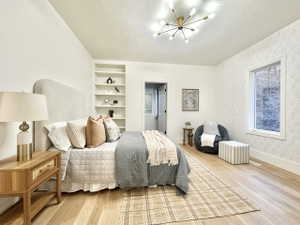 Spacious room featuring wood-finish flooring, a contemporary sputnik chandelier, an accent wall with geometric wallpaper, built-in shelving, and a large window