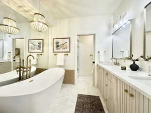 Freestanding soaking tub with a floor-mounted gold-tone faucet, accompanied by dual vanities featuring fluted cabinetry, quartz countertops, and gold-tone hardware