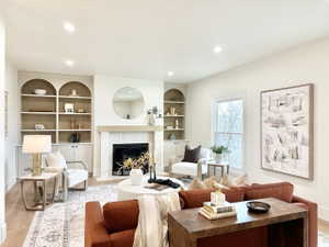 Living space featuring a tiled fireplace with a wood mantle, built-in arched bookcases, and recessed lighting