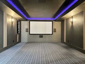 Dedicated media room featuring a large projection screen, integrated wall speakers, and a patterned carpet