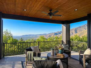 Covered outdoor patio featuring a wood-panel ceiling with recessed lighting and a ceiling fan, black metal railings, and a mountain backdrop