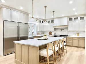Spacious kitchen featuring a large central island with seating, stainless steel appliances, light wood-finish flooring, white shaker-style cabinetry, and pendant lighting