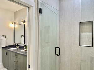 Contemporary bathroom featuring a glass-enclosed shower with a tiled niche and a vanity with a dark countertop, integrated sink, and fluted cabinet doors
