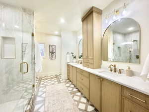Spacious bathroom featuring a frameless glass shower enclosure with marble-finish tile, dual wood-finish vanities with white countertops, and patterned floor tiling