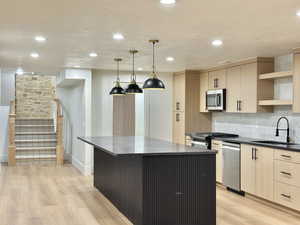 Open-concept kitchen featuring light wood-finish cabinetry, a dark island with a contrasting countertop, stainless steel appliances, and pendant lighting