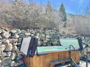 Outdoor spa with a wood-finish cabinet surrounded by a stone retaining wall and natural landscaping