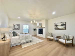Spacious bedroom featuring light wood-finish flooring, a contemporary fireplace with a wood mantel, and an elegant chandelier