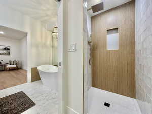 Spacious bathroom featuring a freestanding soaking tub, wood-finish accent wall, and a large shower with a rain showerhead