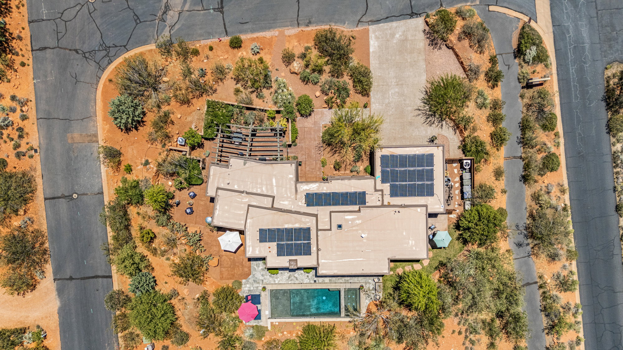 Contemporary residence with multiple rooflines, extensive solar panel arrays, a rectangular swimming pool, and a multi-level patio area