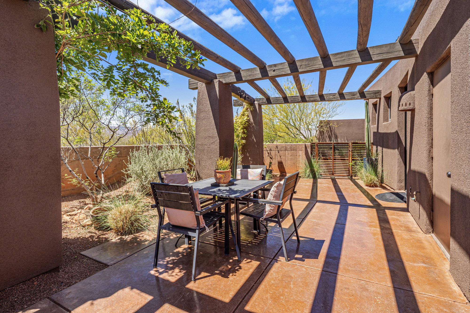 Expansive outdoor patio featuring a wood-beam pergola, stucco exterior, desert landscaping, and a privacy fence