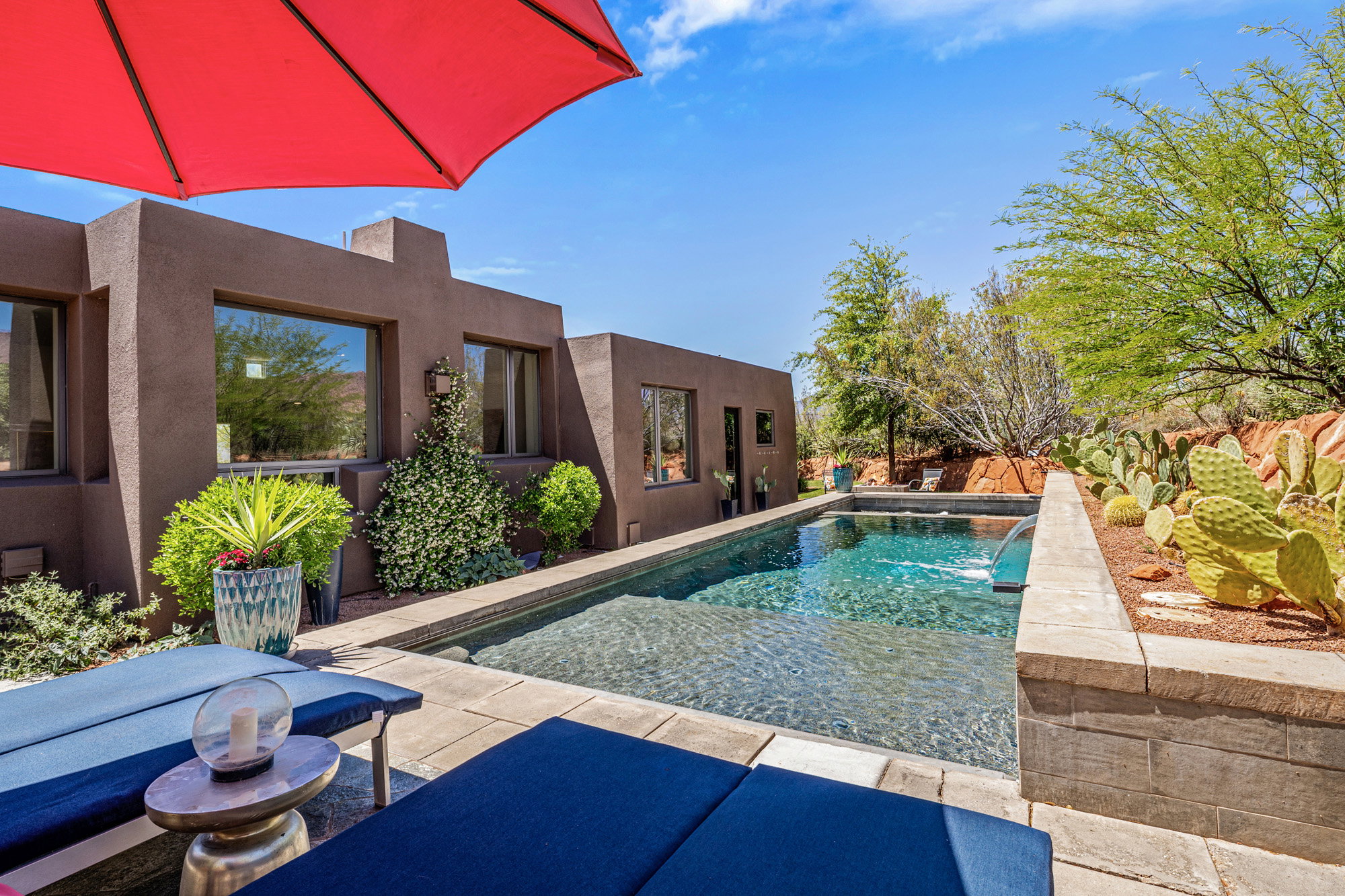 Outdoor pool area featuring a rectangular pool with integrated water feature, surrounded by paver patio and desert landscaping
