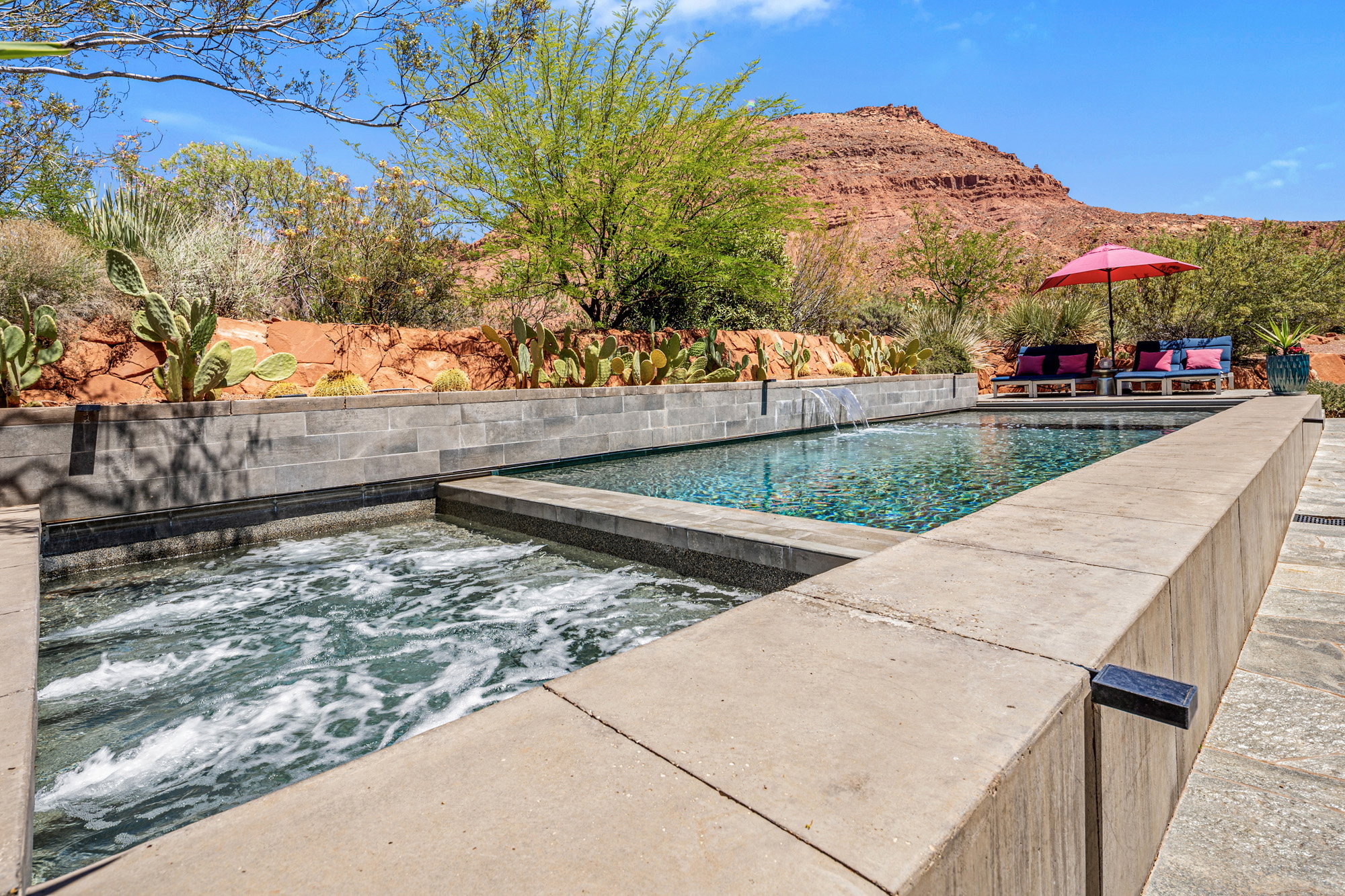 Integrated spa and swimming pool with stone coping and a waterfall feature, set against a desert landscape with natural rock formations and established plantings