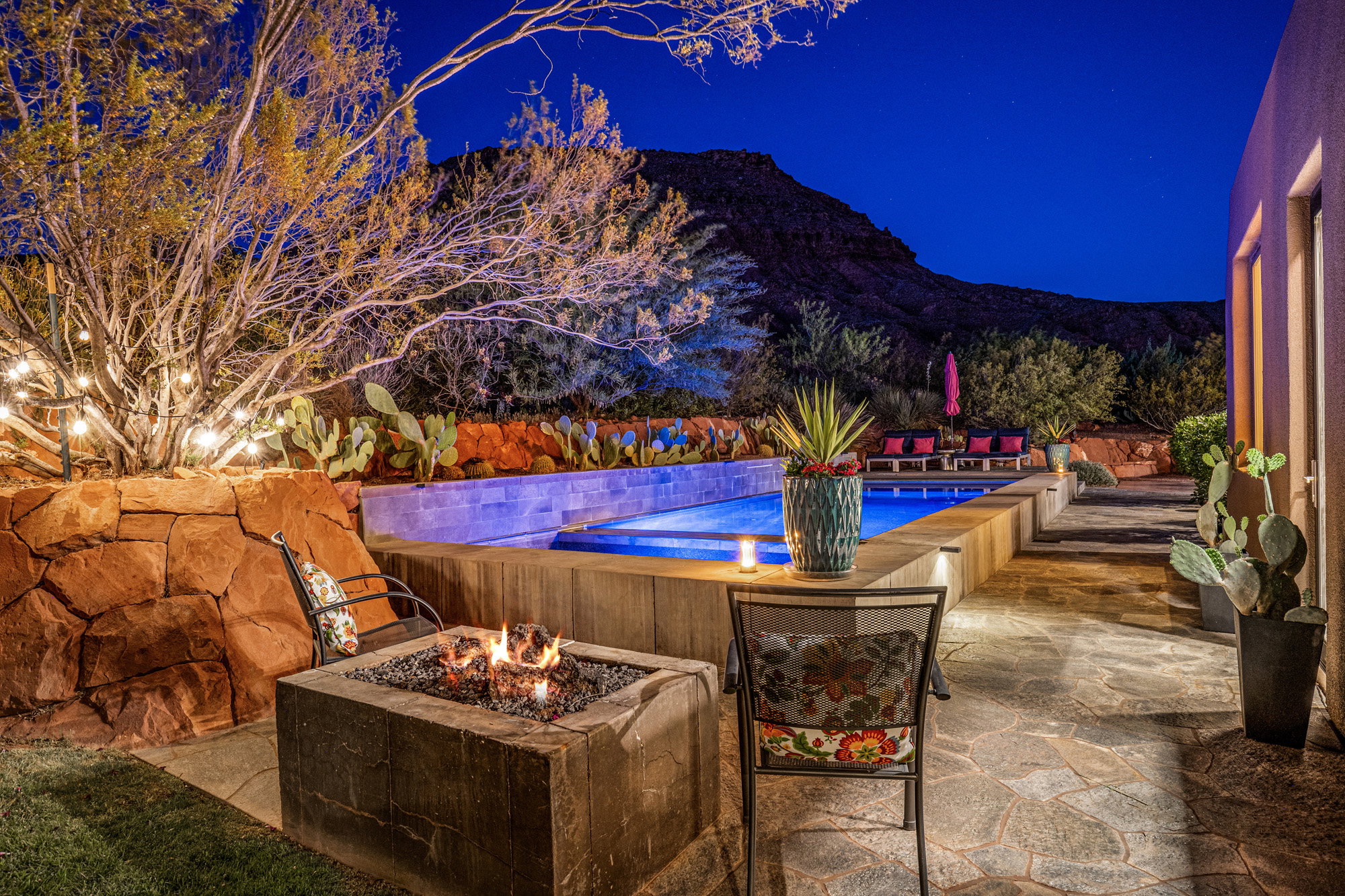 Outdoor living area featuring a built-in fire pit, a swimming pool with integrated lighting, and natural stone patio flooring