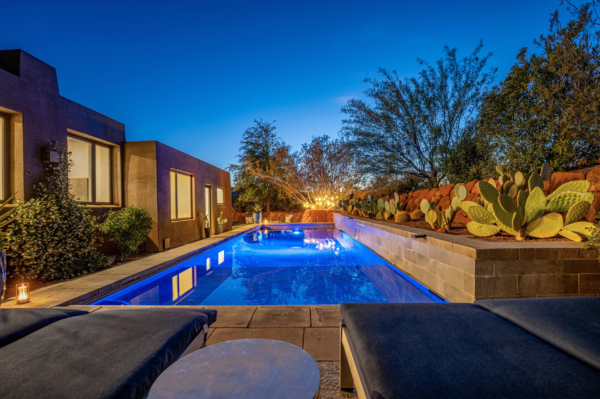 Illuminated swimming pool with integrated spa, bordered by a stone-clad raised planter featuring desert landscaping