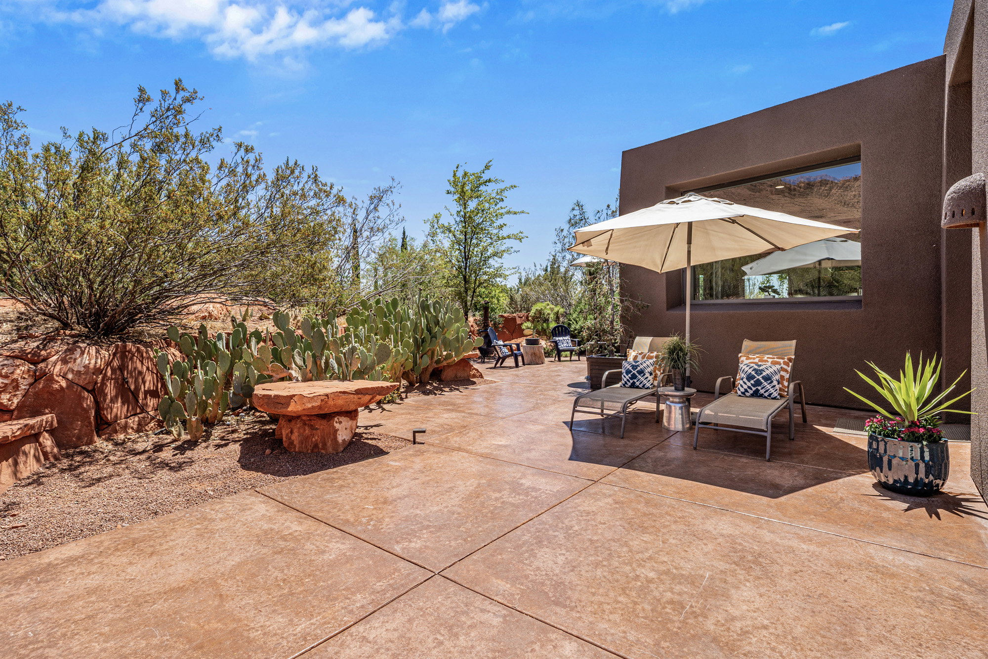 Expansive patio featuring scored concrete flooring, a desert-adapted landscape with rock formations and cacti, and a recessed window