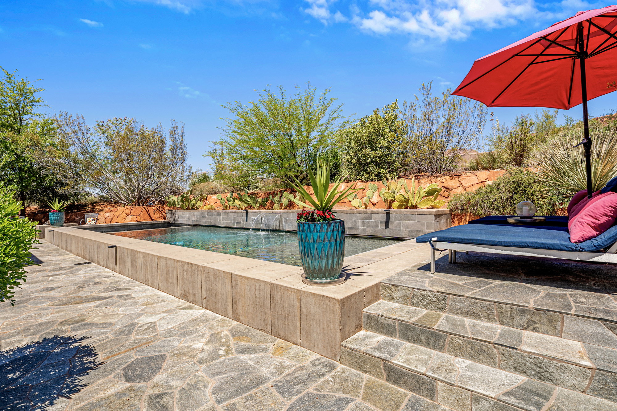 Rectangular swimming pool with water feature, surrounded by flagstone paving and a raised planter bed