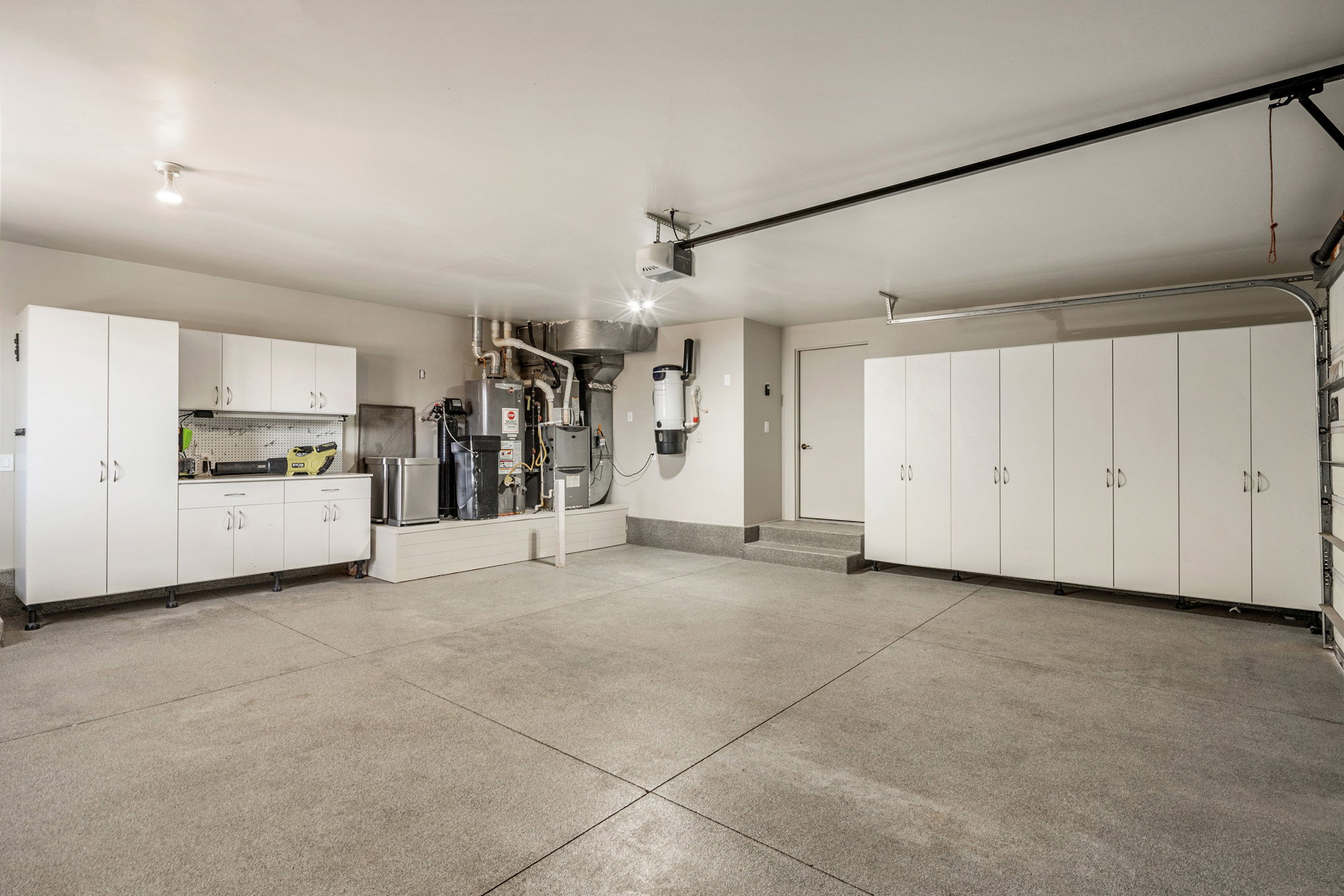Spacious garage featuring a durable epoxy floor, extensive white built-in cabinetry, and a dedicated utility area