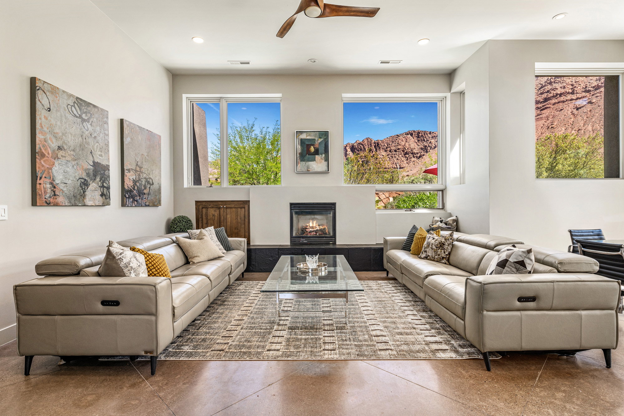 Living area featuring a central fireplace, multiple large windows, recessed lighting, concrete flooring, and a ceiling fan