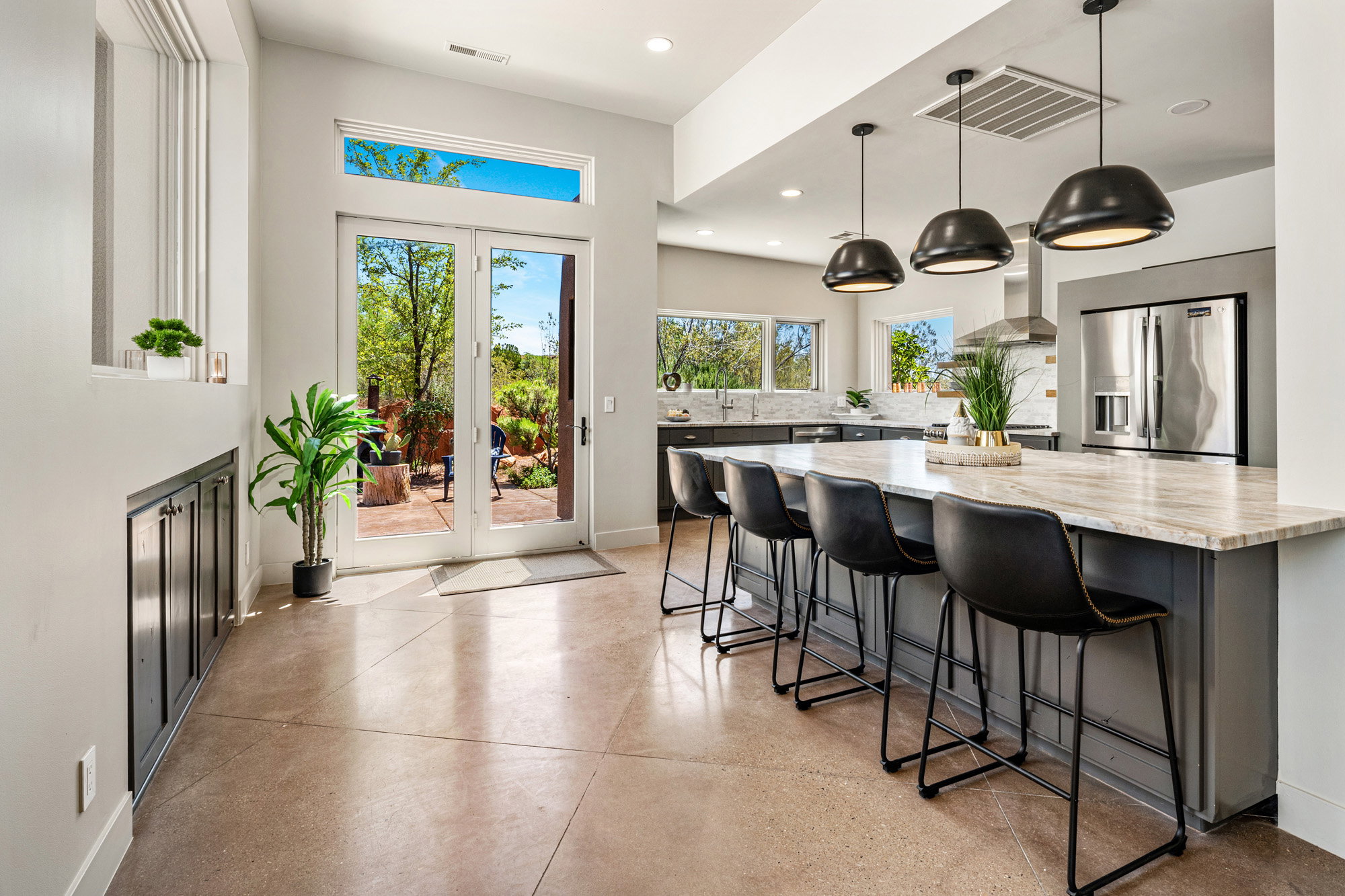 Open-concept living space featuring French doors, a kitchen island with seating for four, three pendant lights, stainless steel appliances, and a tiled backsplash