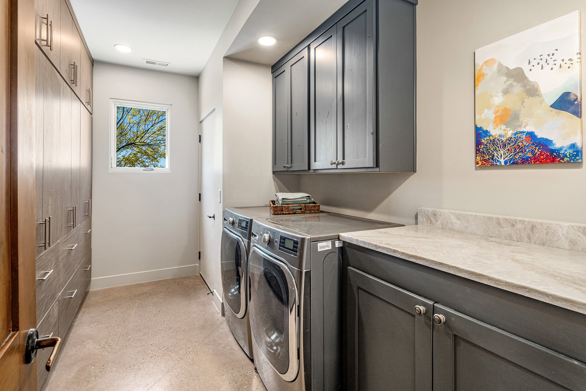Dedicated laundry room featuring wood-finish cabinetry, integrated washer and dryer, grey shaker-style upper and lower cabinets, light-toned countertop, and recessed ceiling lighting