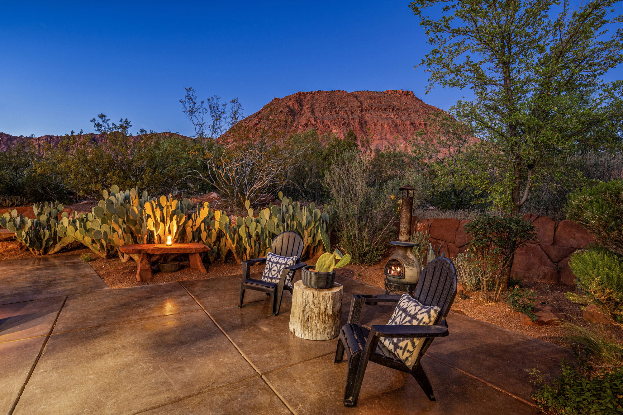 Spacious outdoor patio with concrete flooring, surrounded by desert landscaping and a stone retaining wall