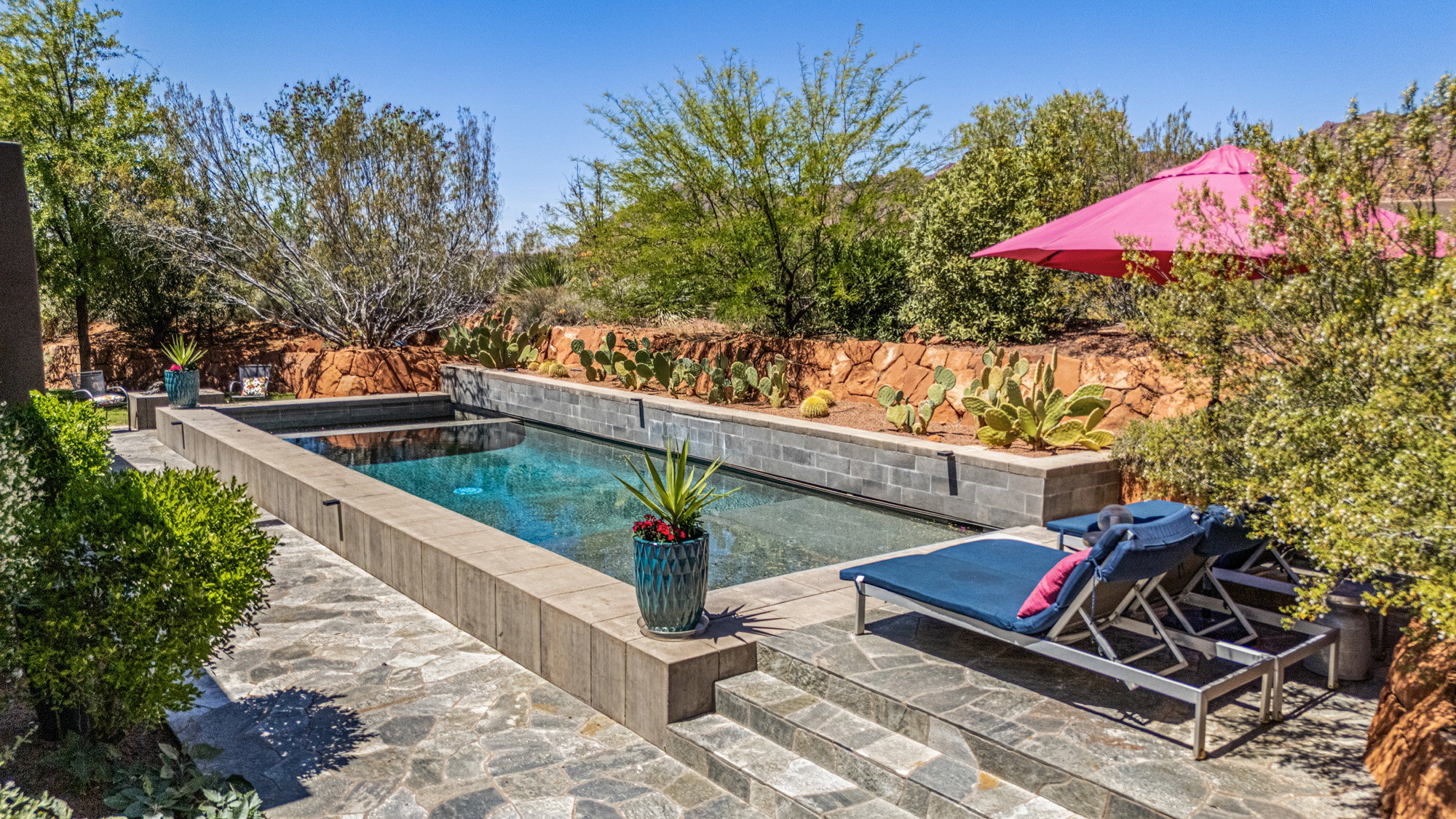Rectangle swimming pool with an integrated spa, surrounded by flagstone paving and tiered landscaping featuring desert flora