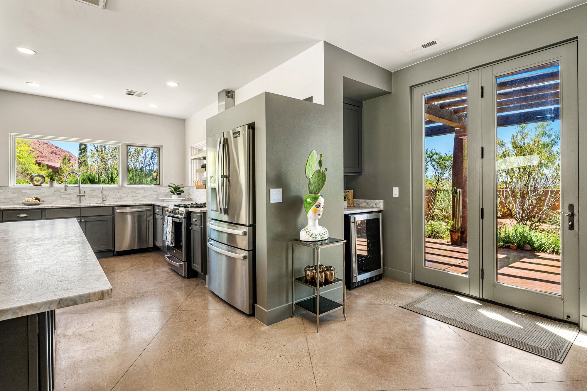 Kitchen with light-toned concrete flooring, stainless steel appliances, dark cabinetry, and light-toned countertops