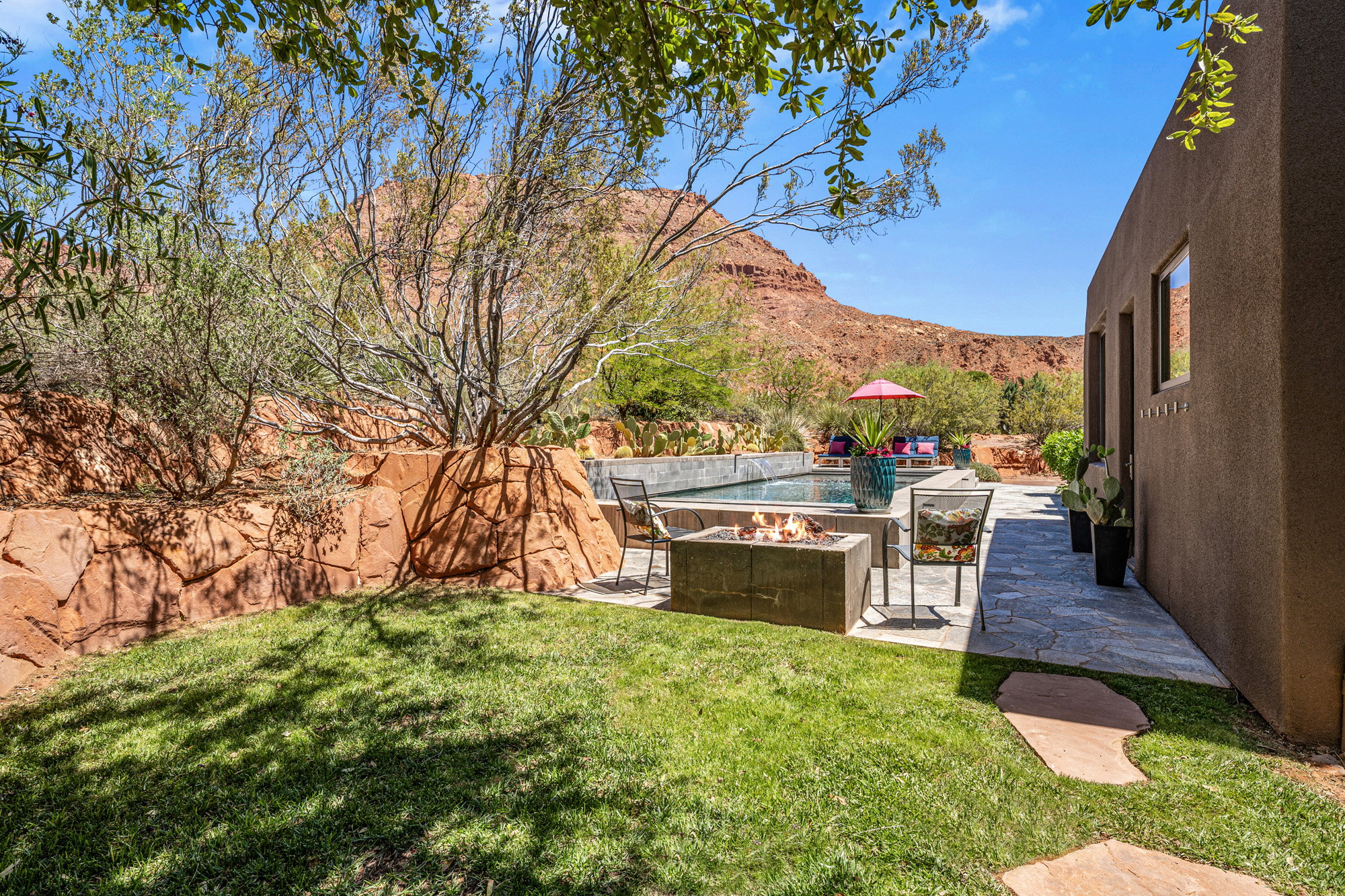 Expansive backyard featuring a manicured lawn, stone paver patio, built-in fire pit, and a swimming pool