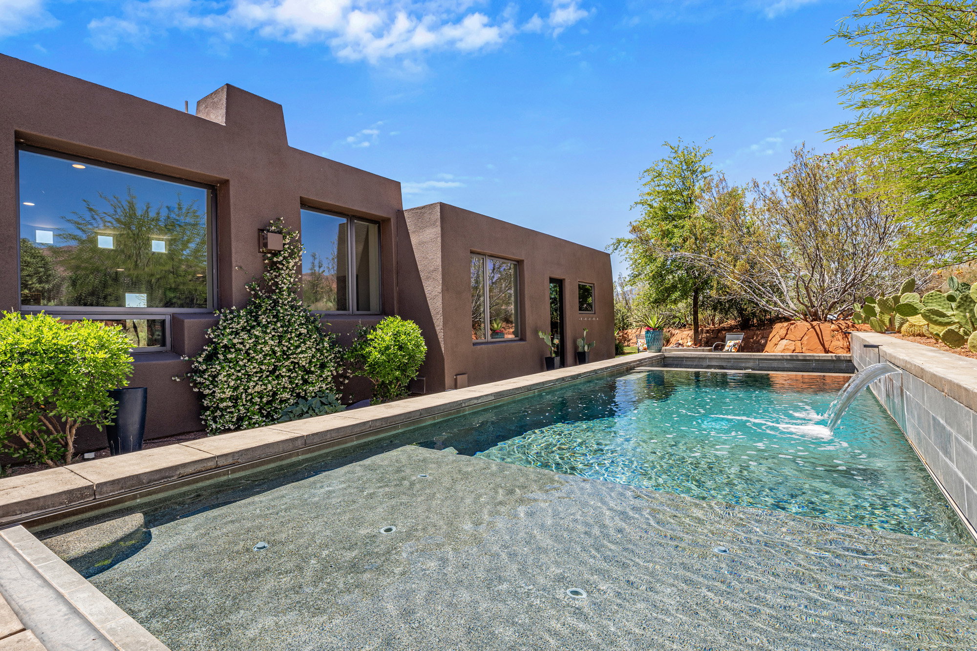 Contemporary brown stucco exterior with multiple windows, an integrated swimming pool, and an in-pool spa