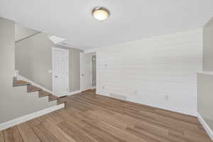 Spacious room featuring wood-finish flooring, a shiplap accent wall, and a staircase with coordinating wood-finish treads