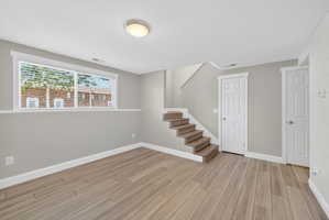 Spacious room with wood-finish flooring, a large window, and light gray wall paint