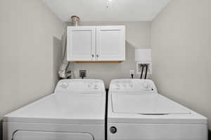 Dedicated laundry area featuring overhead white shaker-style cabinetry, light gray walls, and a textured ceiling