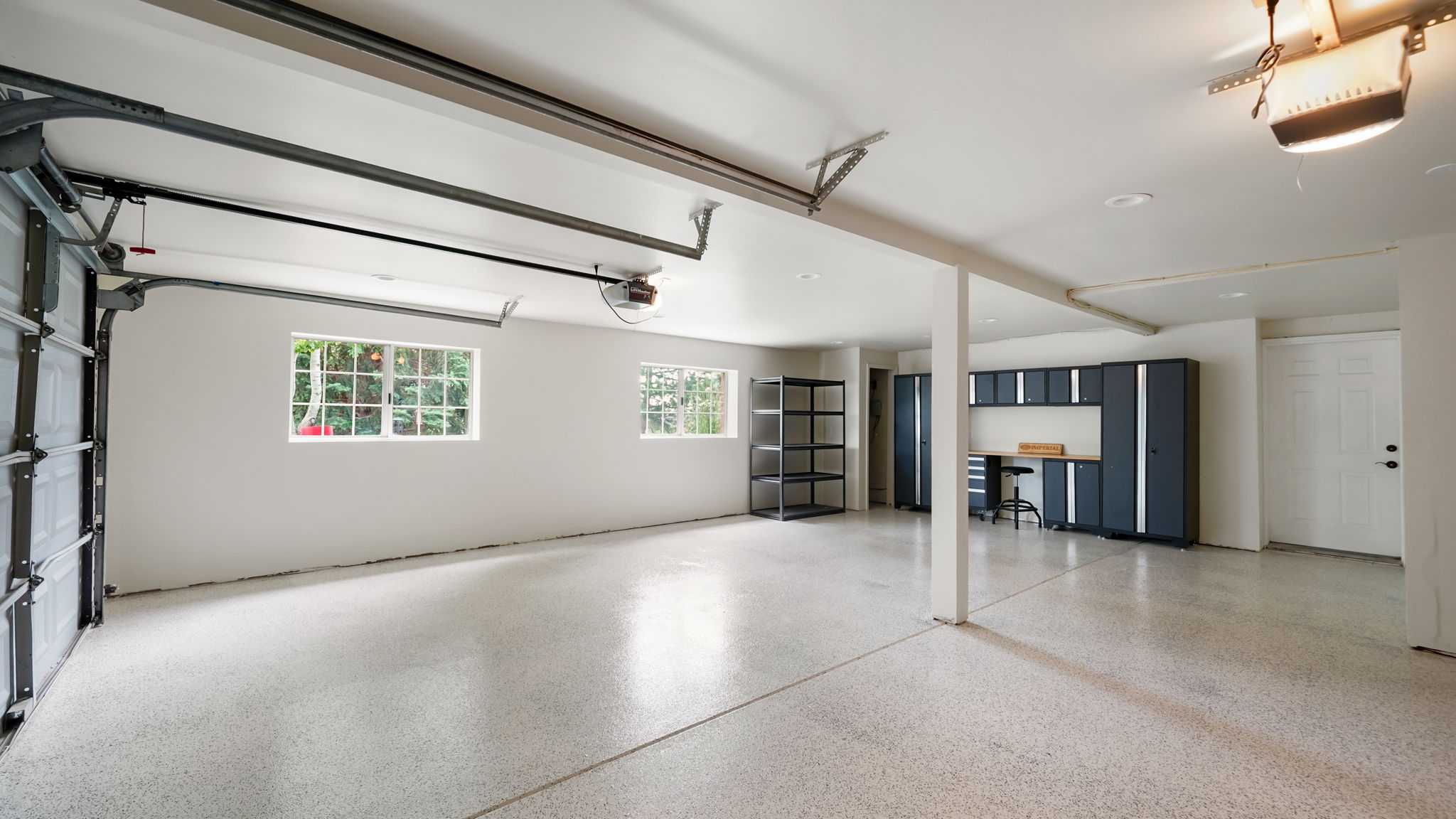 Spacious garage with an epoxy-coated floor, multiple windows, built-in cabinetry, an integrated workbench