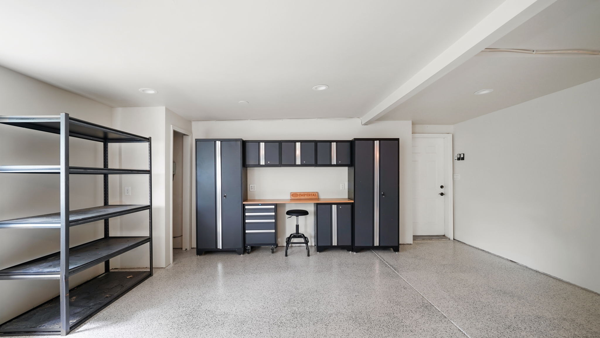 Spacious garage with epoxy flooring, built-in Spacious garage with an epoxy-coated floor, multiple windows, built-in cabinetry, an integrated workbench, wood-finish countertop, recessed lighting, and shelving unit