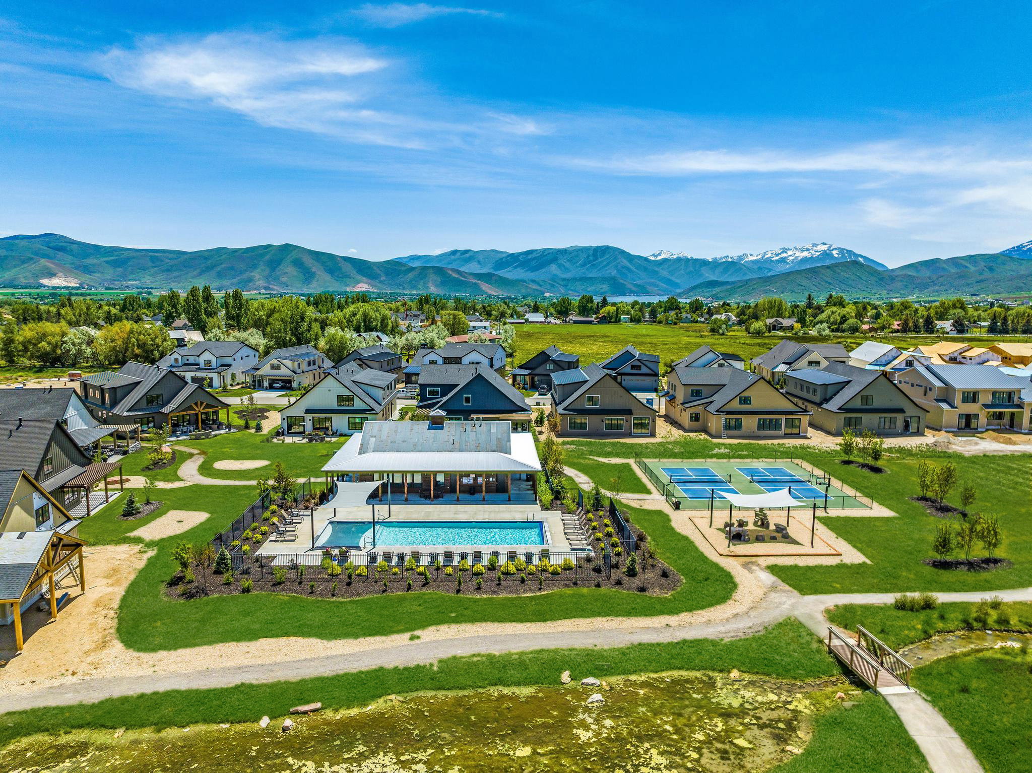 Community amenities including a swimming pool with covered lounge area, multiple sports courts, and a pedestrian bridge over a natural water feature