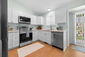 Kitchen featuring white cabinetry, light-toned countertops, stainless steel appliances, and wood-finish flooring