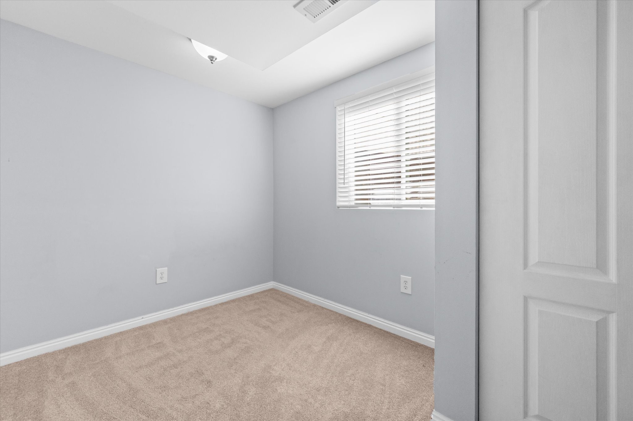 Neutral toned room featuring light gray walls, plush carpeting, and a window with blinds