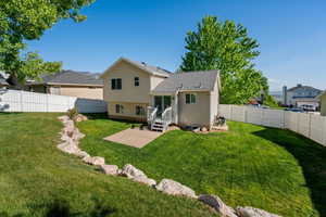 Expansive grassy yard featuring a multi-level house exterior with siding, a white privacy fence, a concrete patio, and a deck with stairs