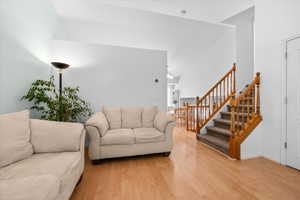 Open concept living space featuring vaulted ceilings, wood-finish flooring, and a staircase with wood banisters and carpeted treads