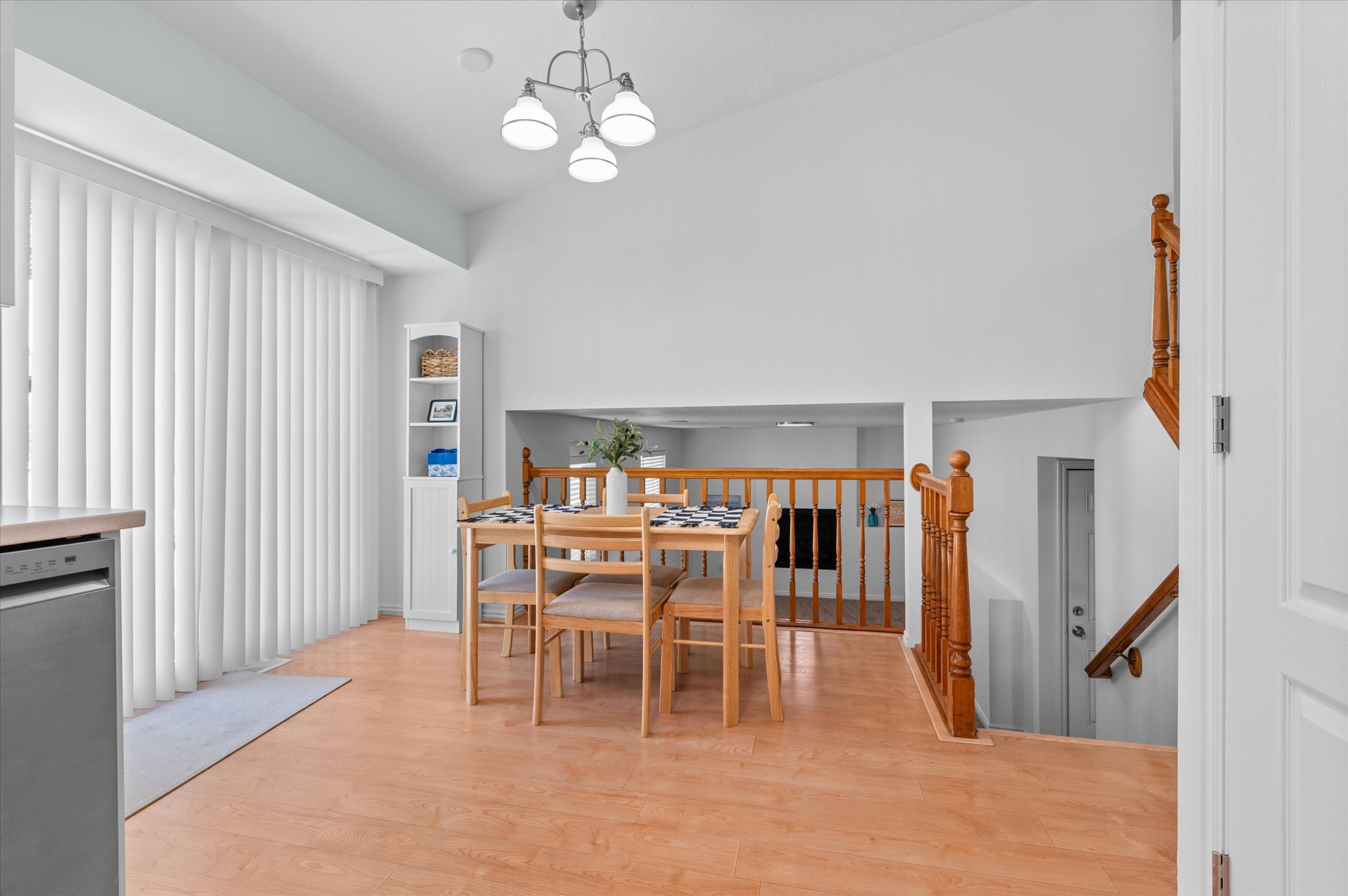Vaulted ceilings accent this dining area with wood-finish flooring, a contemporary chandelier, and shelving unit