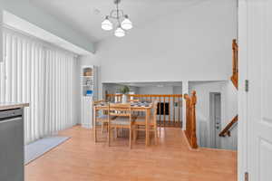 Vaulted ceilings accent this dining area with wood-finish flooring, a contemporary chandelier, and shelving unit