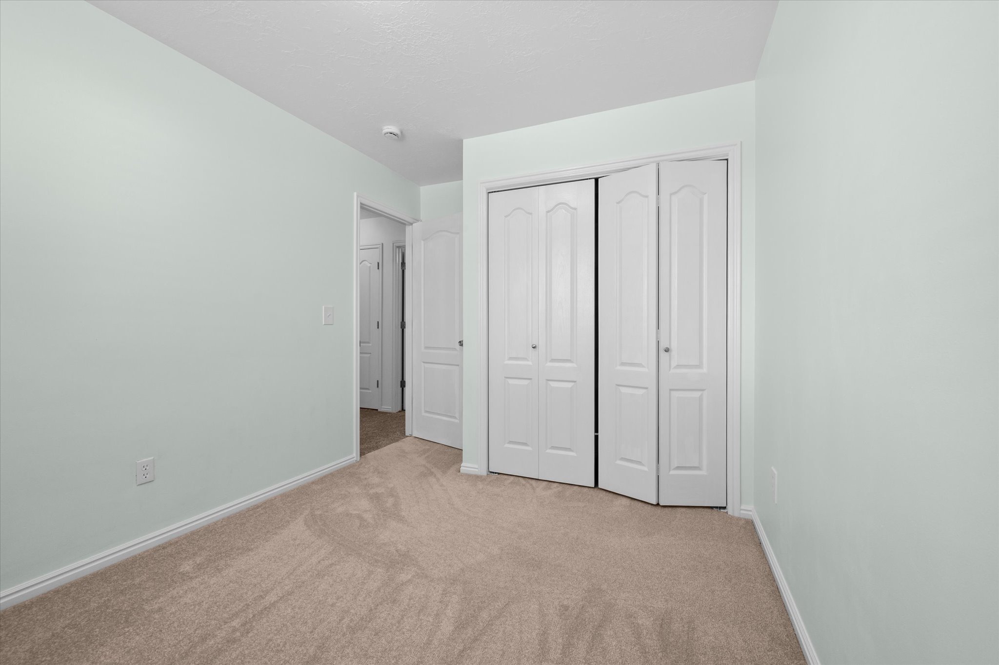 Carpeted room featuring light green walls, white baseboards, and bi-fold closet doors with panel detailing