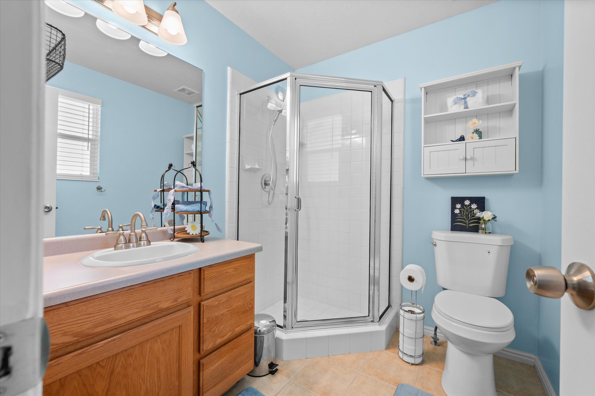 Bathroom featuring a corner shower enclosure, a single vanity with a laminate countertop, a large wall mirror, and a wall-mounted storage cabinet